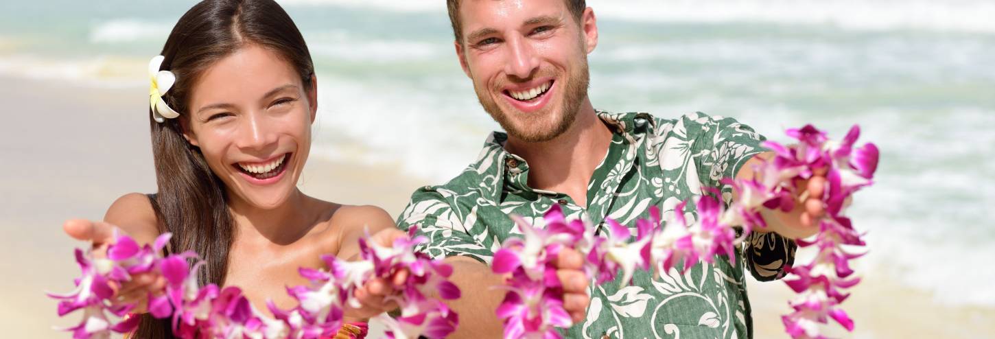 A couple wearing floral shirts smile at their wedding on Poipu Beach in Kauai