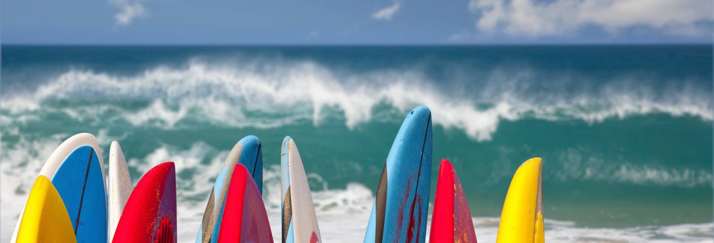 Surfboards standing upright on the Kauai beach, with a crashing Pacific wave in the background