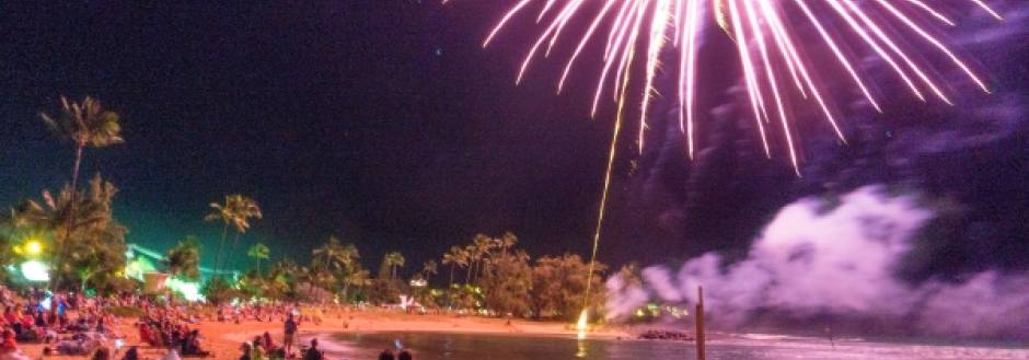 A crowd sits along Poipu Beach in Kauai and watches a New Years Eve fireworks display over the Pacific